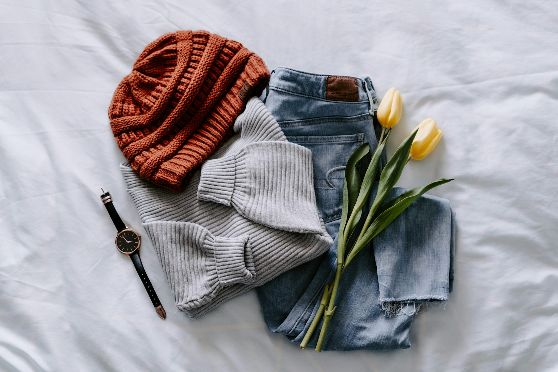 Folded knitwear, denim, and flowers arranged as a casual capsule.